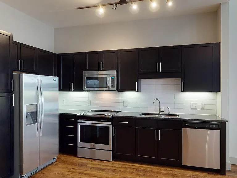 Apartment kitchen with stainless steel appliances, granite countertops and wood-style flooring.