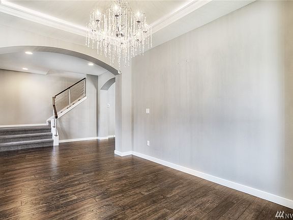 Formal dining room offers tray ceiling with crown molding, arched doorway, chandelier, and engineered hardwood floors. 