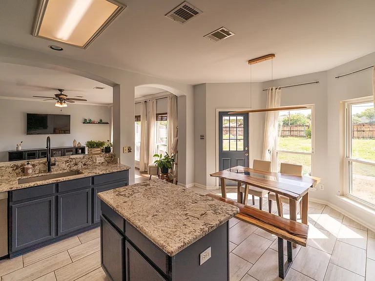 Chef's Kitchen with Premium Finishes: Prepare meals with ease in this stylish kitchen boasting chic navy cabinets, durable granite countertops, a central island, and modern stainless steel appliances. The tile flooring ensures easy cleanup.