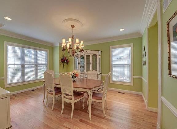 Dining room with wood floor, chair rail, box window, triple crown molding, and both recessed lighting and chandelier.