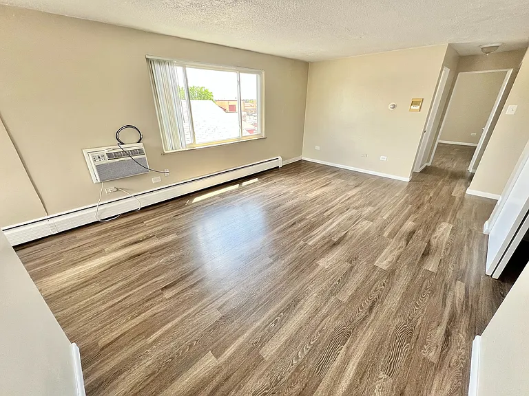 Bright and airy living room with modern wood flooring, large window, and sleek AC unit, offering a warm and inviting atmosphere.