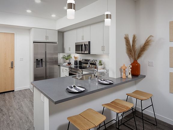 model kitchen with a large island with two stools and a stainless steel refrigerator