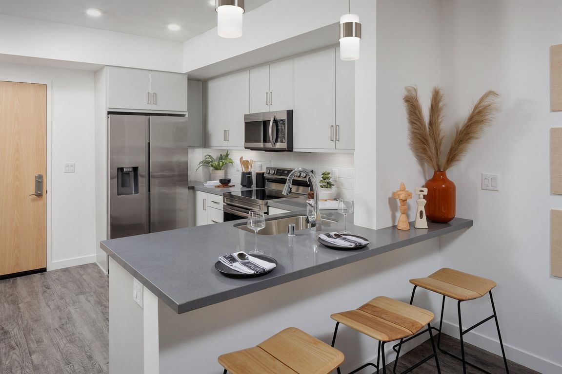 model kitchen with a large island with two stools and a stainless steel refrigerator