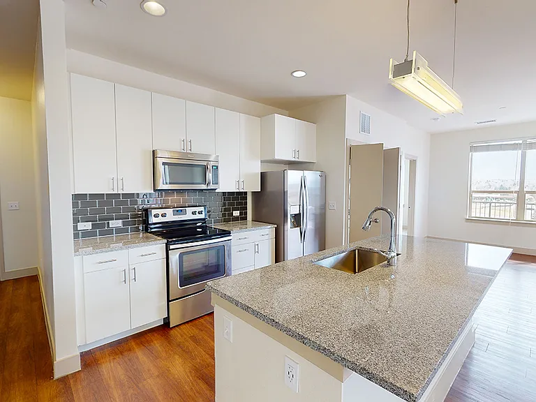 Apartment kitchen with stainless steel appliances, granite countertops and wood-style flooring.