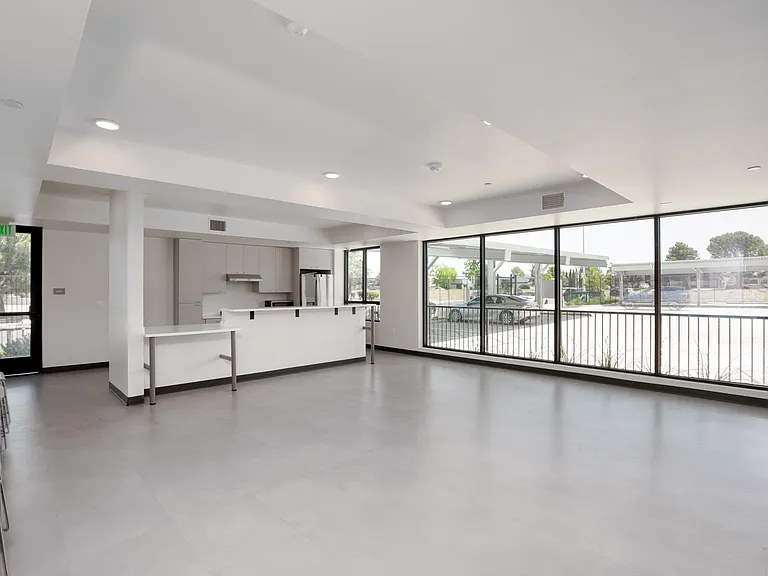 Spacious community room with floor to ceiling windows, open layout, and an adjacent kitchen perfect for gatherings and events.