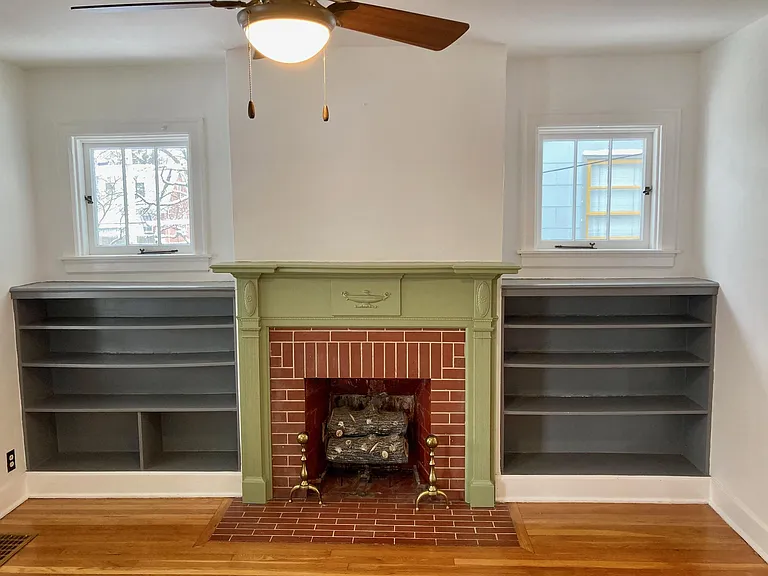 Classic architecture of the period with a brick fireplace, wooden mantle, built-in bookshelves and matching windows.