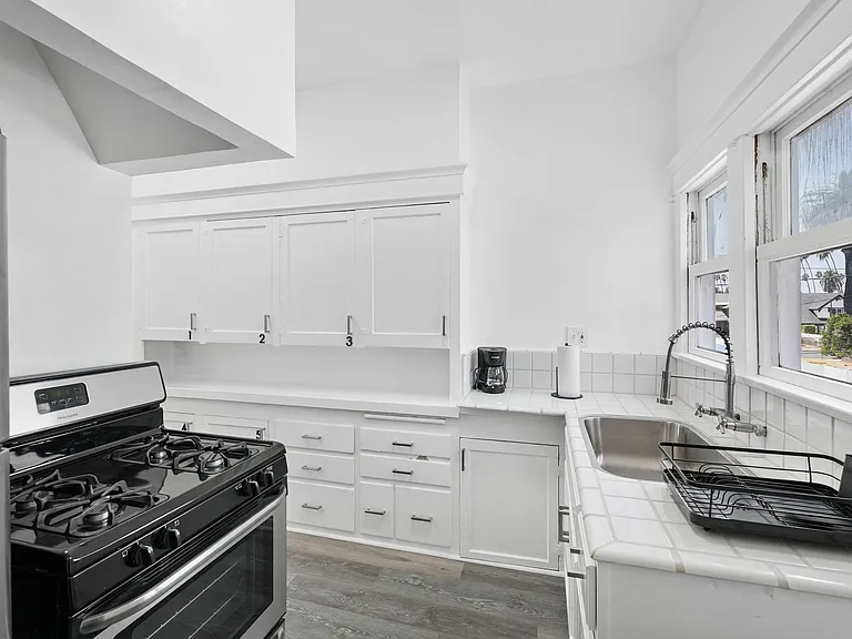Kitchen features a gas range, ample cabinet storage, and generous counter space with a double sink by the window.