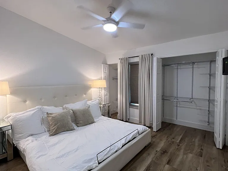 Spacious bedroom with a ceiling fan, large closet with built-in shelving, and a window dressed with full curtains.