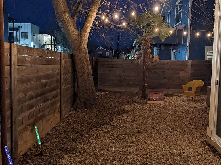 Fenced in backyard with cozy string lights (night view)