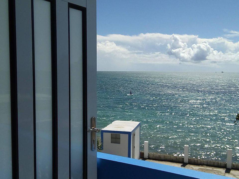 Seafront balcony entry to the house at the open floor plan living-dining-kitchen area which has a brand new powerful 20,000 BTU split air conditioning system, ceiling fans and 50 inch Smart TV with remote controls.