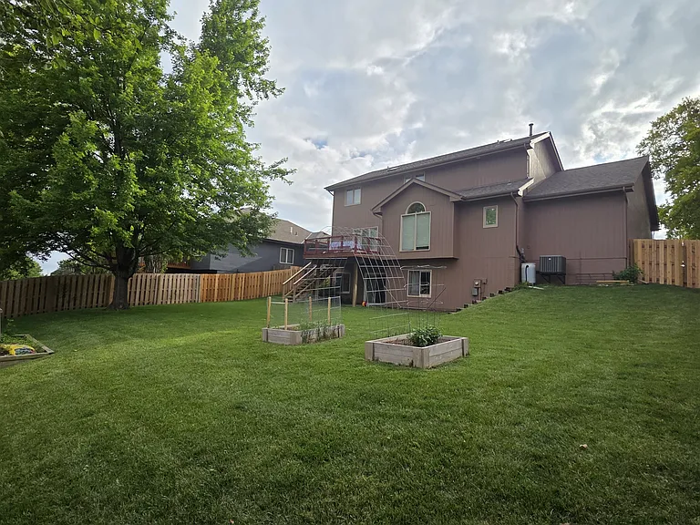 Backyard featuring large lawn, deck with sliding door to kitchen, walkout basement, and raised garden beds.