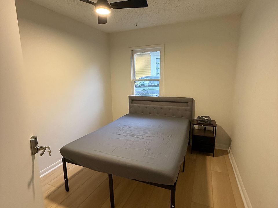 Simple bedroom with a ceiling fan, wood-look flooring, and a window for natural light, plus space for a nightstand.