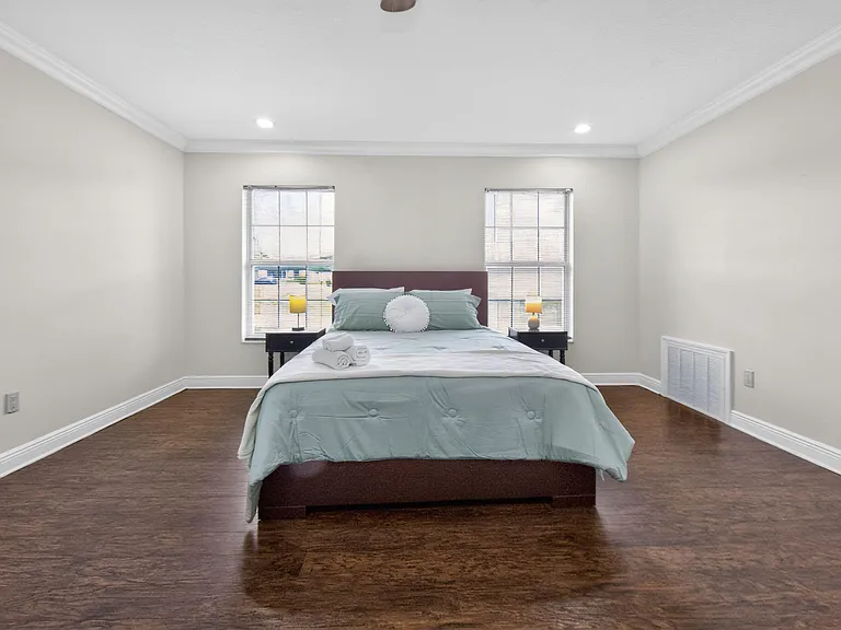 Spacious bedroom with hardwood floors, crown molding, and two large windows for natural light, plus space for nightstands.