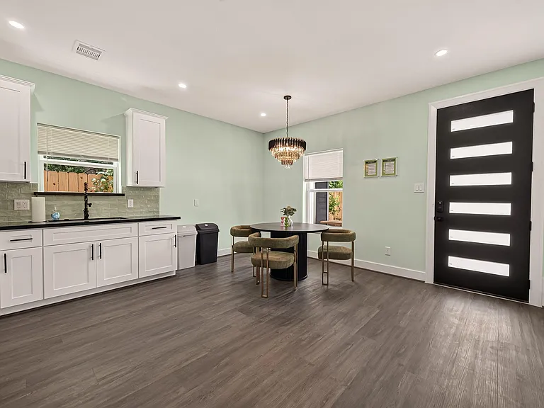 Open kitchen and dining area with shaker cabinetry, tile backsplash, and a dining nook near windows and the entry.