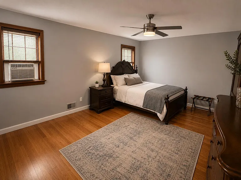 Well-appointed bedroom with hardwood floors, ceiling fan, dual windows, and a furnished layout with nightstand and dresser.