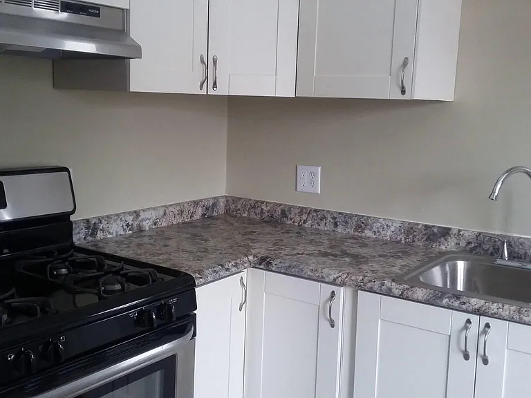 Close up of new countertops, kitchen sink, stove, vent, and cabinets