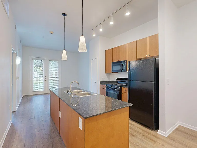 Apartment kitchen with dark counters and wood style floors.