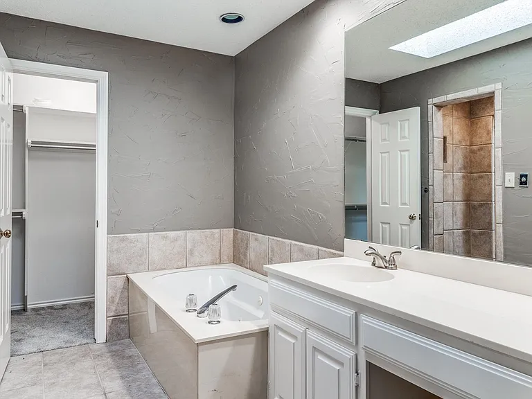 Other half of master bath with vanity seating, tub and view into master closet and shower