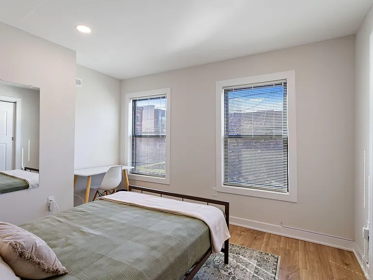 Furnished bedroom with two windows, a comfortable bed, and a compact desk area for work or study.
