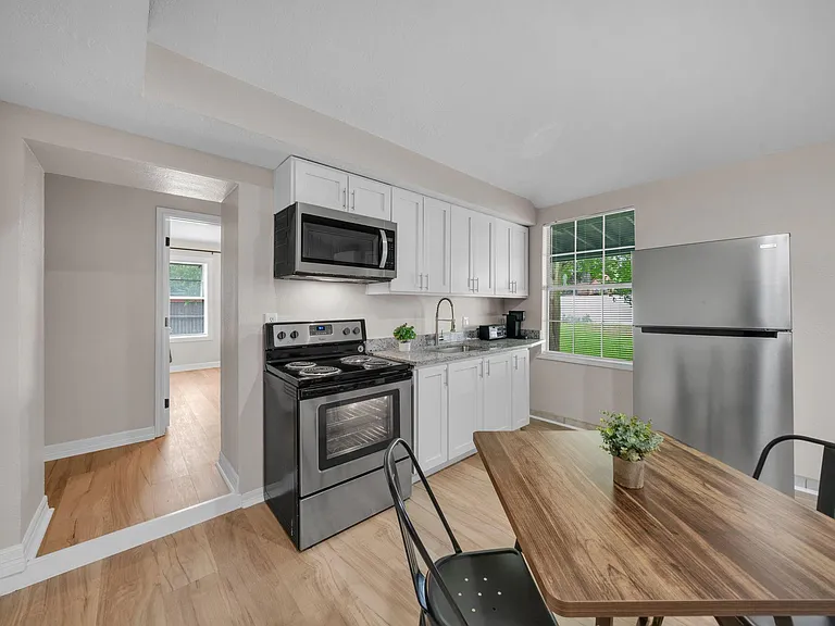 Updated kitchen with white cabinetry, granite-look counters, stainless fridge, and electric range plus a window over the sink