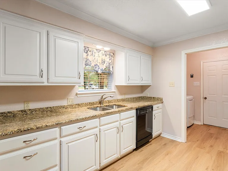 Kitchen featuring wood-finish flooring, white cabinetry, granite-style countertops, an undermount double basin sink, and a black dishwasher