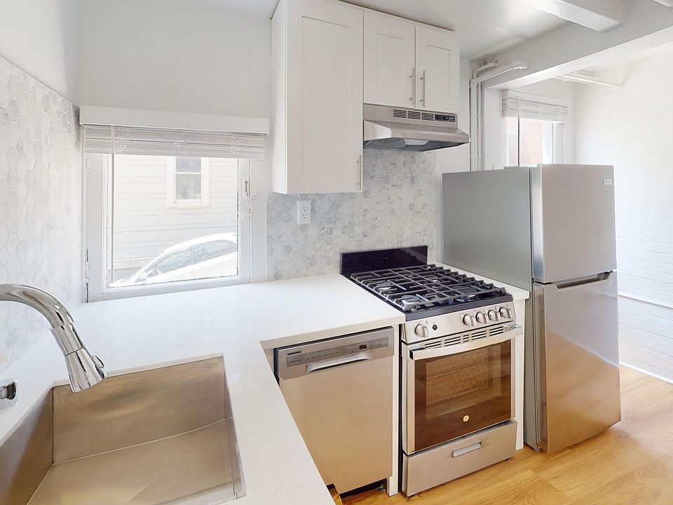Kitchen with multiple cabinets, refrigerator, stove, range hood, and sink