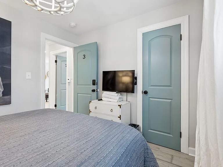 Private bedroom with a comfortable bed, wall-mounted TV, dresser storage, and easy access to the hallway.