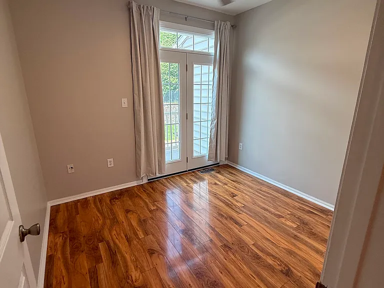A bright and versatile second bedroom with rich wood flooring, a modern ceiling fan, and French doors leading to the private balcony. An ideal space for guests, a home office, or everyday living.