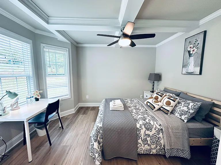 Well-appointed bedroom with tray ceiling, ceiling fan, and desk area, plus large windows and nightstand storage.