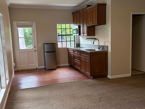 Kitchen with wood cabinets. Microwave, fridge, stovetop. Space for small table. Wood floor. 
No oven.