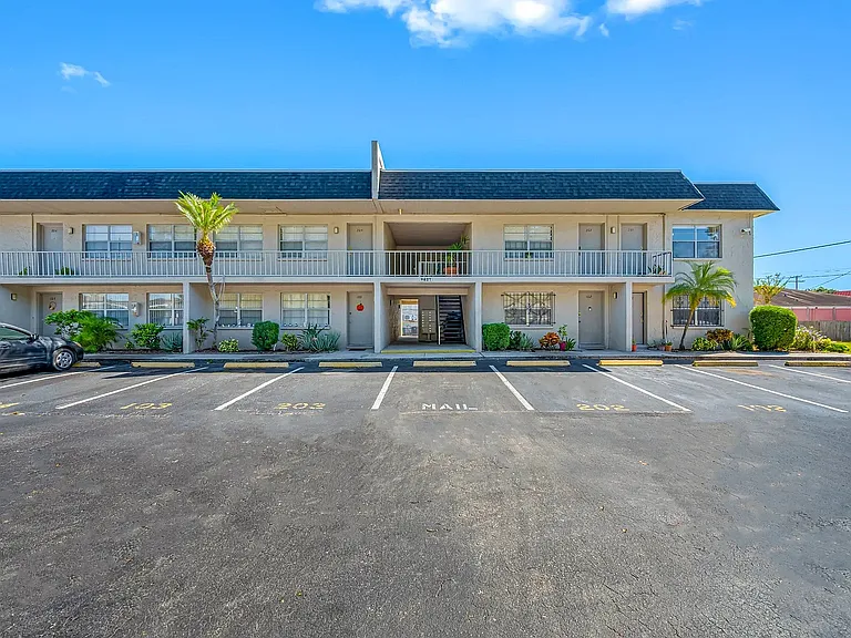 Charming two-story apartment building with lush landscaping and convenient parking, under a clear blue sky.