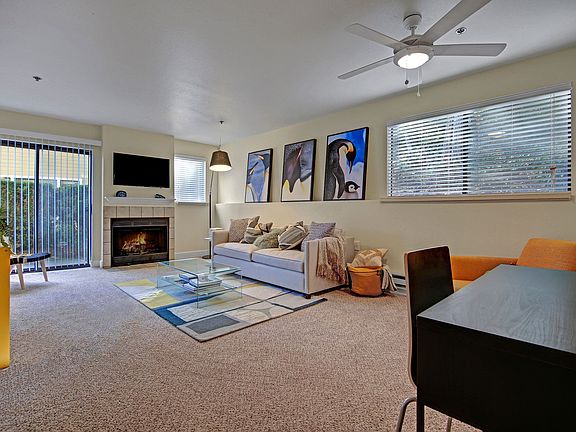 Living room with couch, desk, armchair, large windows, ceiling fan, fireplace, and sliding glass door out to a patio