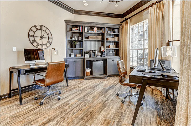 Business center with book shelf, two desks with computers, and wood-style flooring