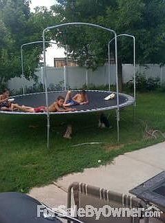 The kids turn on the sprinklers and get on the tramp on a hot summer day.