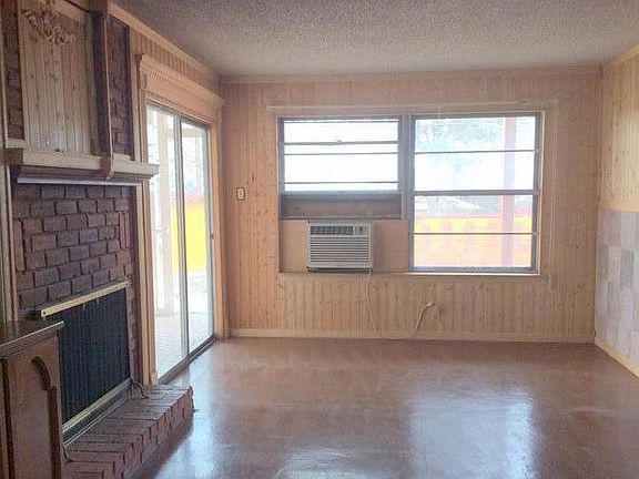 The family room has sliding glass doors onto the back porch, a brick fireplace, glass front china cabinet and dining area to the right side of this photo. The AC unit was removed when the new central heat and air were installed.