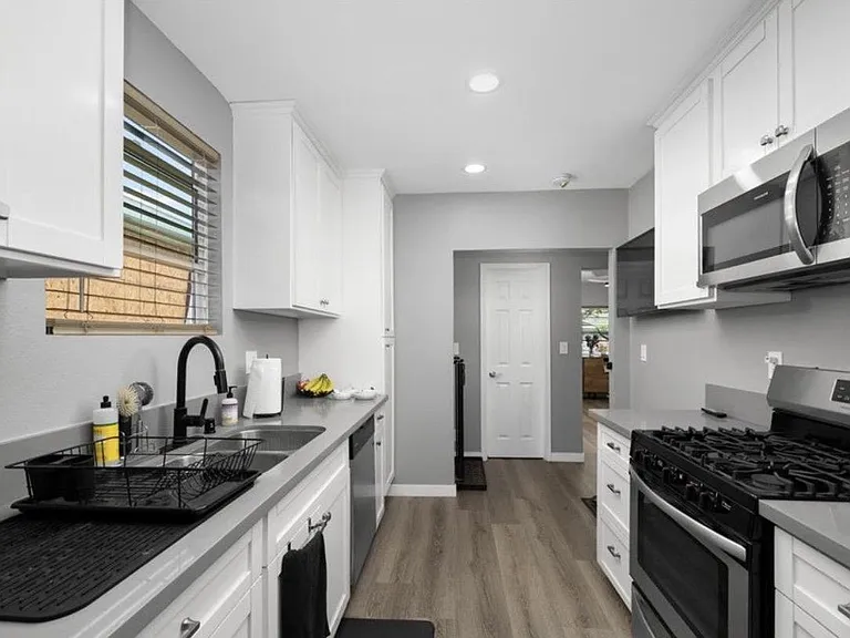 Galley kitchen with white cabinetry, ample counter space, gas range, built-in microwave, and a large sink under a window.