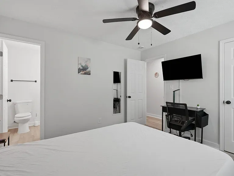 Well-kept bedroom with a ceiling fan, wall-mounted TV, and dedicated desk area, plus convenient access to an en-suite bath.