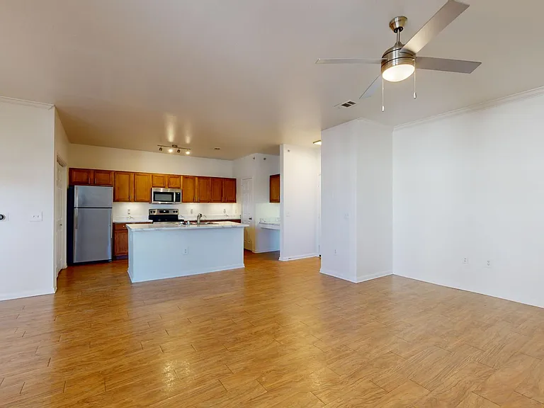 Apartment kitchen with stainless steel appliances, dining and living room with wood-style flooring.