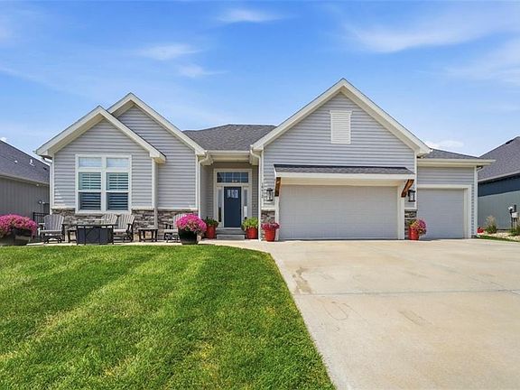 Light grey siding exterior with stone accents, featuring a two-car garage, concrete driveway, and a covered front entry