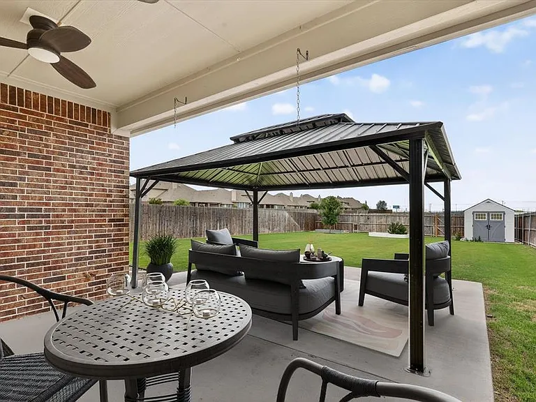 Covered patio featuring a ceiling fan, brick exterior, concrete flooring, and a metal gazebo
