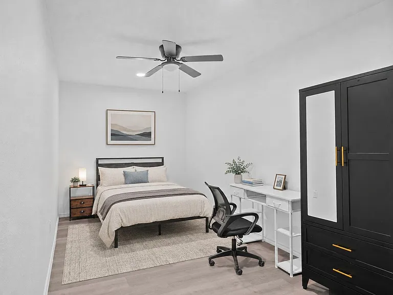 Furnished bedroom with a queen bed, nightstand lighting, dedicated desk workspace, and wardrobe storage with mirrored doors.