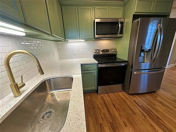 Beautiful tile backsplash with shiny countertops, under cabinet lighting, brand new everything. Look at that huge sink and brass faucet.