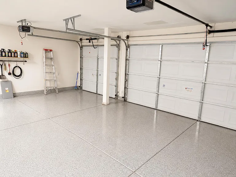 Clean, oversized garage with durable coated flooring, built-in wall storage, and two automatic roll-up doors.