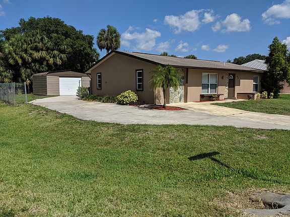North side view of the house and garage. Driveway wraps around to a full concrete patio behind the house to the detached garage, wired for 110 or 220. The yard is completely fenced in for animals or young children.