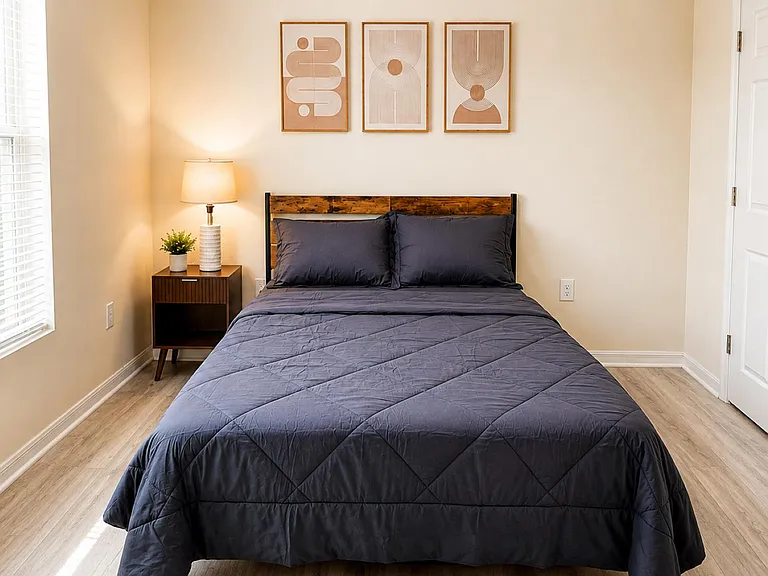 Furnished bedroom with a comfortable full/queen bed, nightstand lighting, and a large window with blinds for privacy.