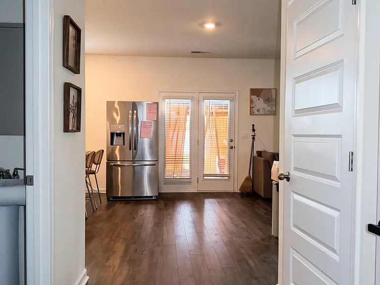 Open common area with durable wood-look flooring, stainless-steel refrigerator, and patio doors with blinds.