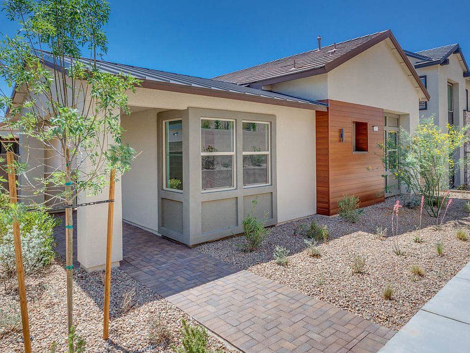 A modern, single-story house with a paved walkway leading to the entrance, surrounded by lush greene