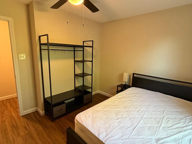 Furnished bedroom with wood-look flooring, ceiling fan, and a full bed plus open storage and nightstand.