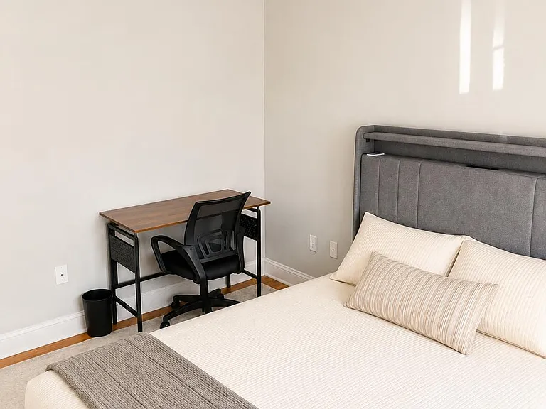 Well-appointed bedroom with a comfortable queen bed, dedicated desk, and a large window with blinds for natural light.