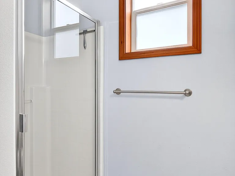 Updated bathroom with a glass-enclosed shower, wood-look flooring, and a large window for natural light and ventilation.